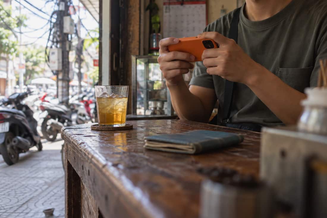 Cánh tay cầm điện thoại ốp lưng cam quay về ống kính, tờ lịch mờ phía sau