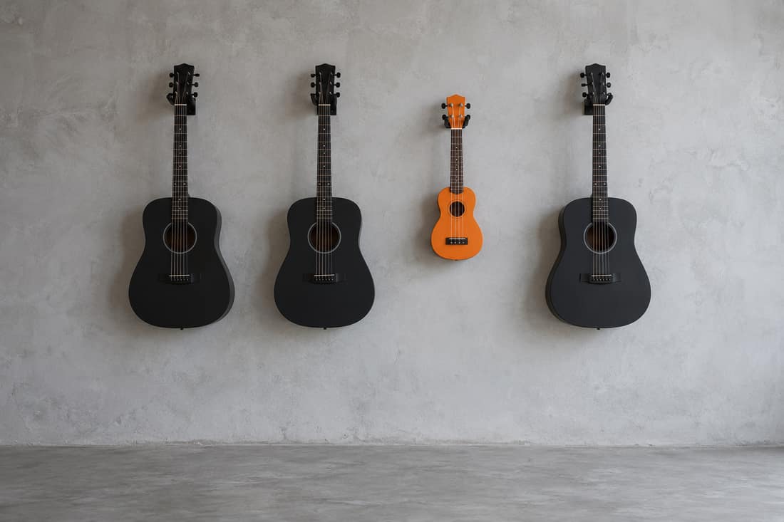 Tiệm bán đàn vắng, ba cây guitar đen và một ukulele màu cam treo thẳng hàng trên tường