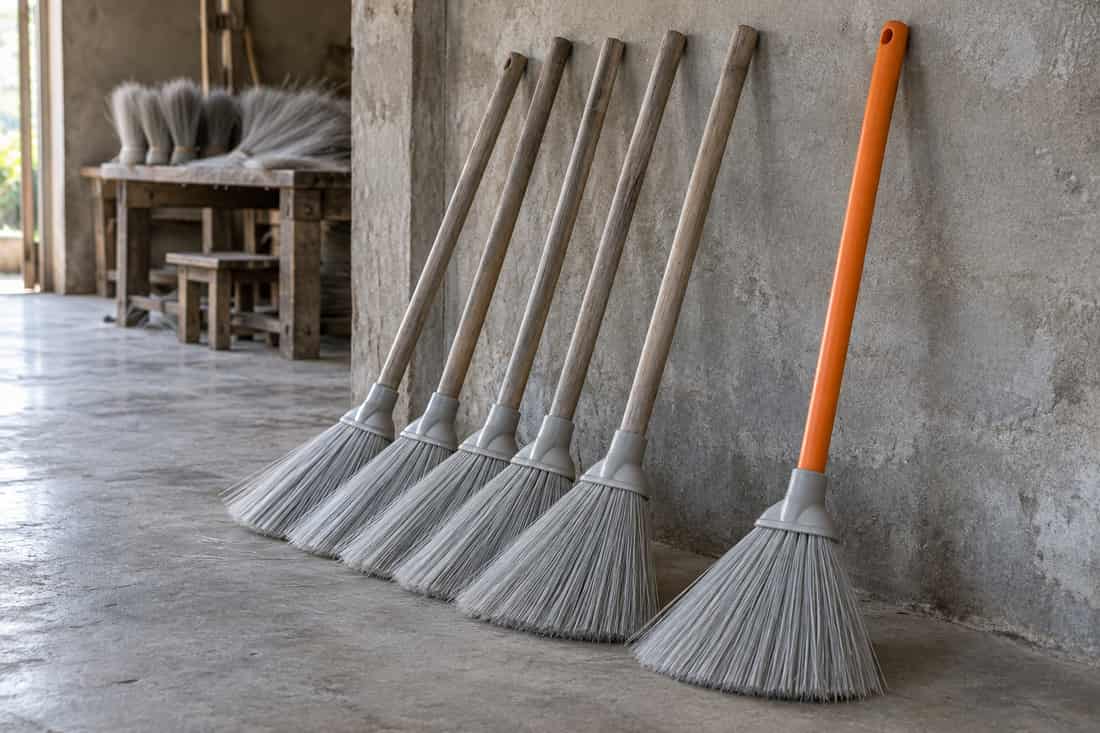 Năm cây chổi cán xám tựa tường thành cụm, một cây chổi cán cam đứng riêng cách cụm một khoảng